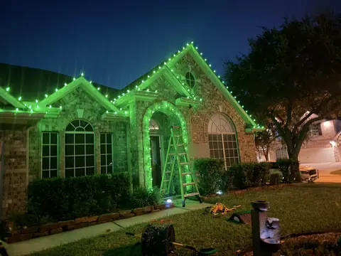 Green C9 lights going up on a brick home at night, ladder still in place