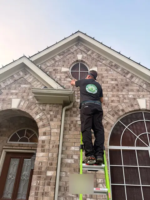QuietScapes installer in a logo shirt on a ladder clipping lights to the roofline